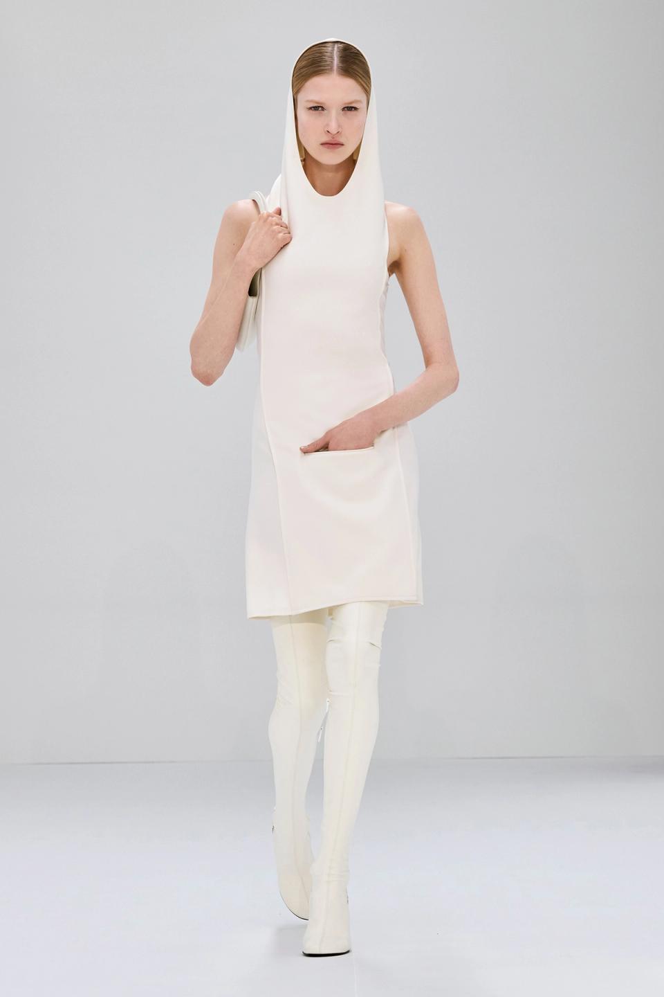 Elegant white dress and thigh-high boots from Courrèges showcased on a runway model.