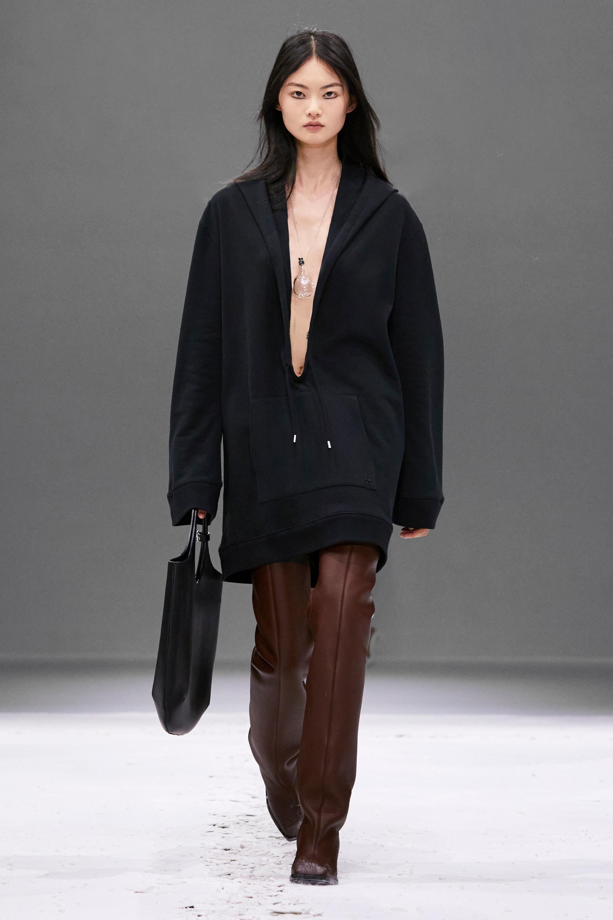 Elegant fashion runway model wearing Courrèges black oversized hoodie and brown leather pants.