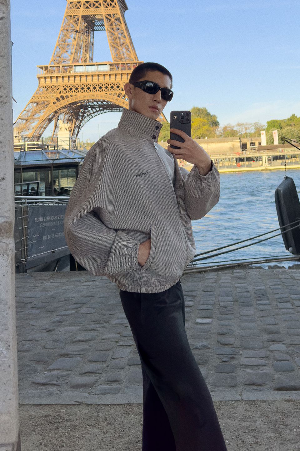 Stylish young person in Courrèges fashion, taking a mirror selfie with Eiffel Tower backdrop.