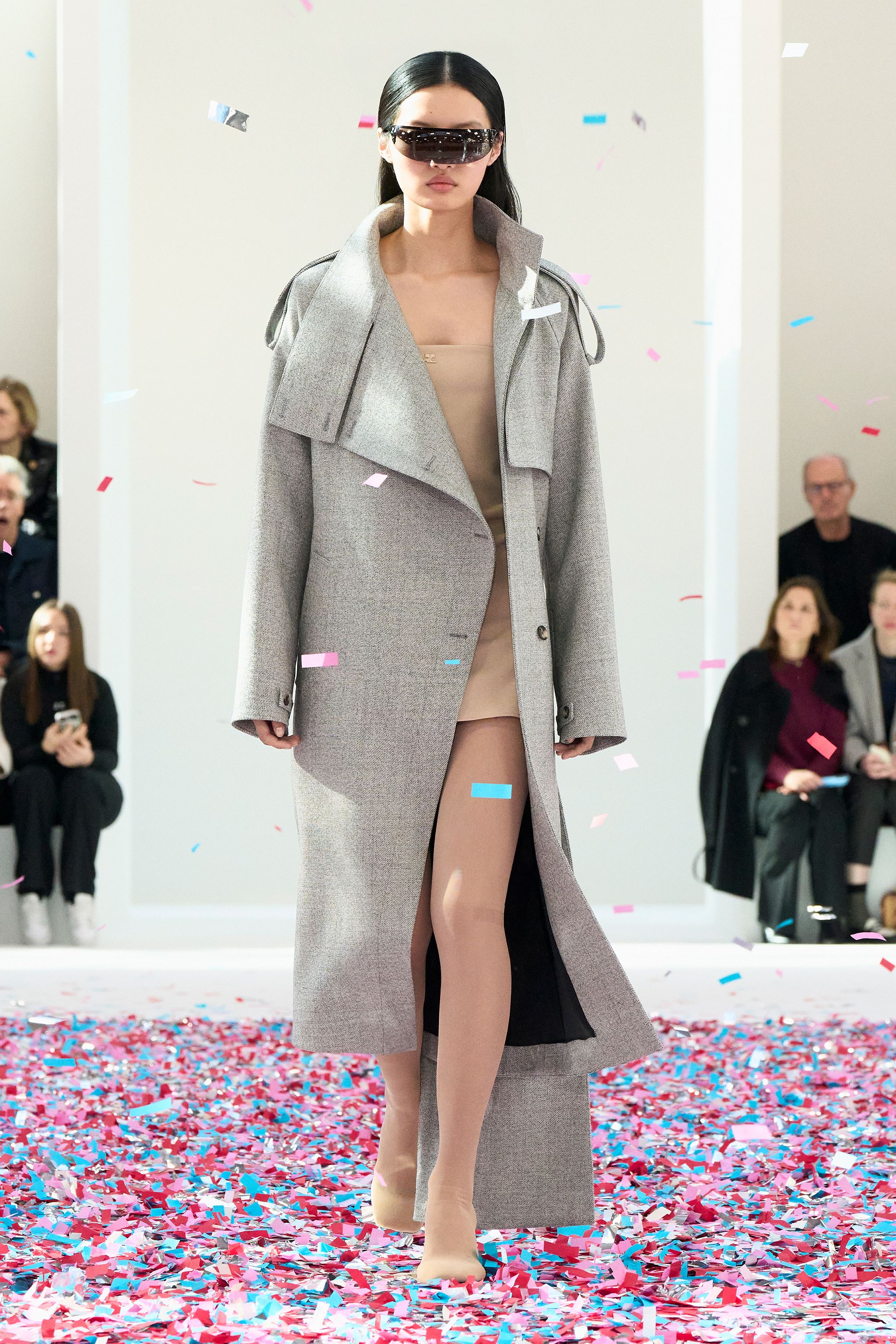 Elegant model in futuristic oversized coat and sunglasses at Courrèges fashion show.