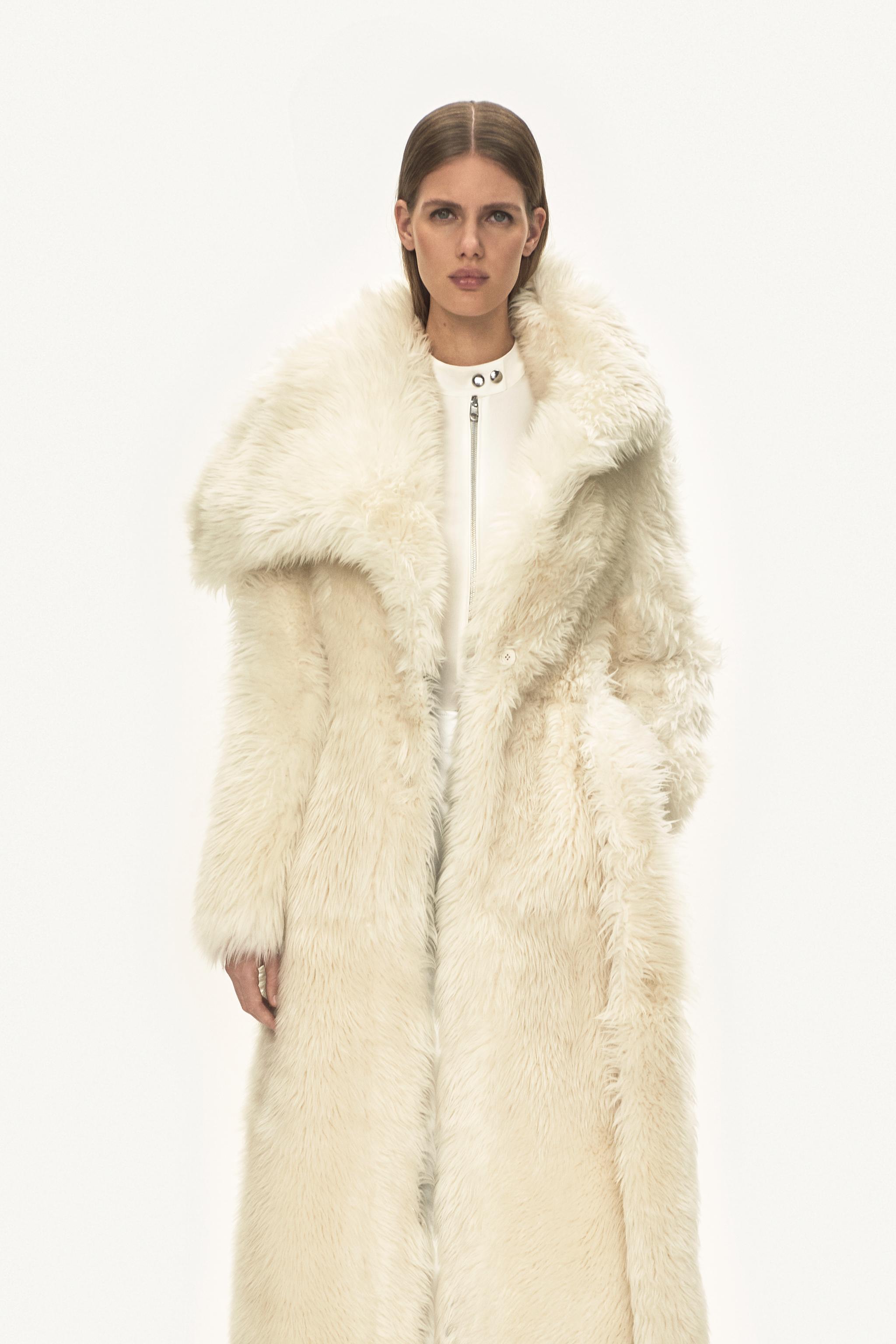Modèle élégant portant un manteau en fourrure synthétique blanche de luxe, représentant Courrèges dans un fond minimaliste.