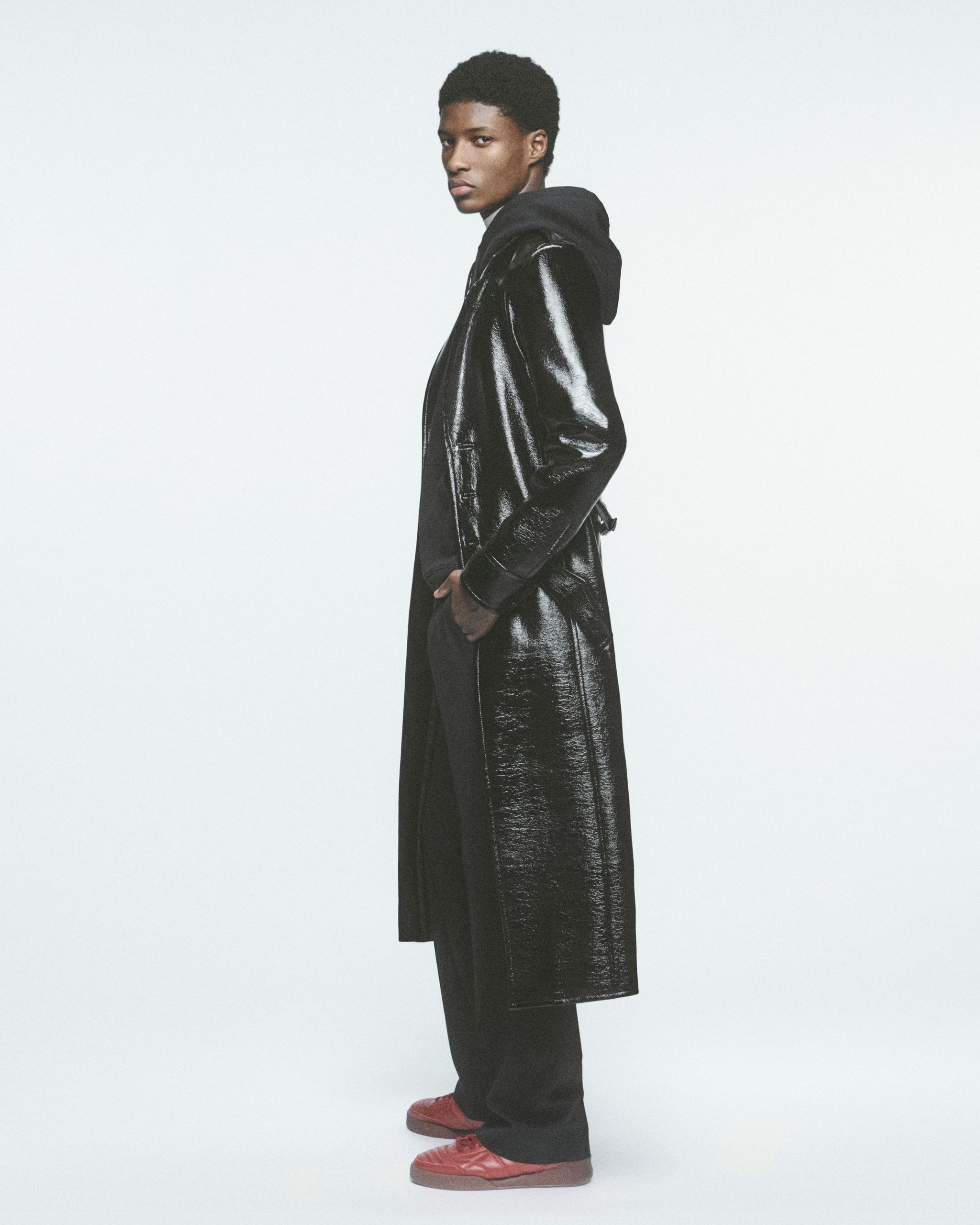 Modèle portant un trench noir élégant et des sneakers décontractés, représentant Courrèges.