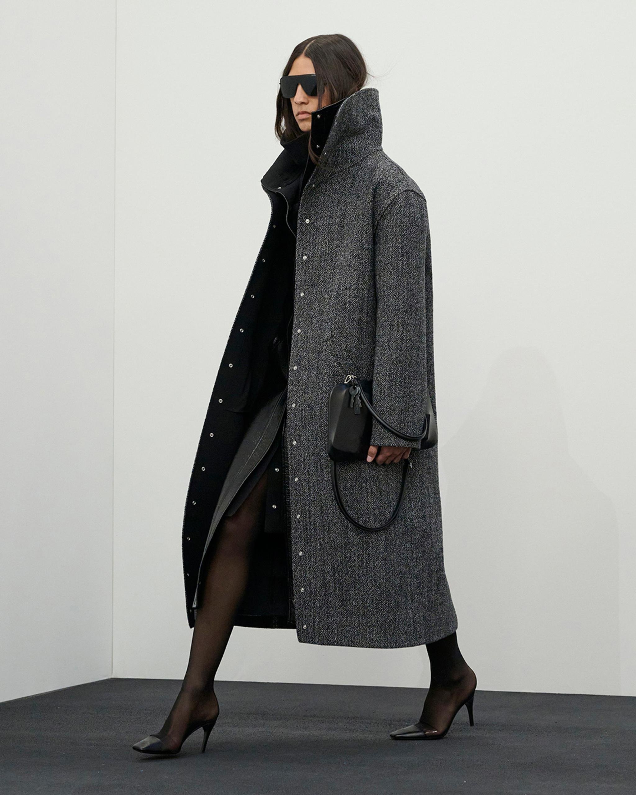 Elegant woman in a long grey coat, black dress, and high heels, showcasing Courrèges fashion.
