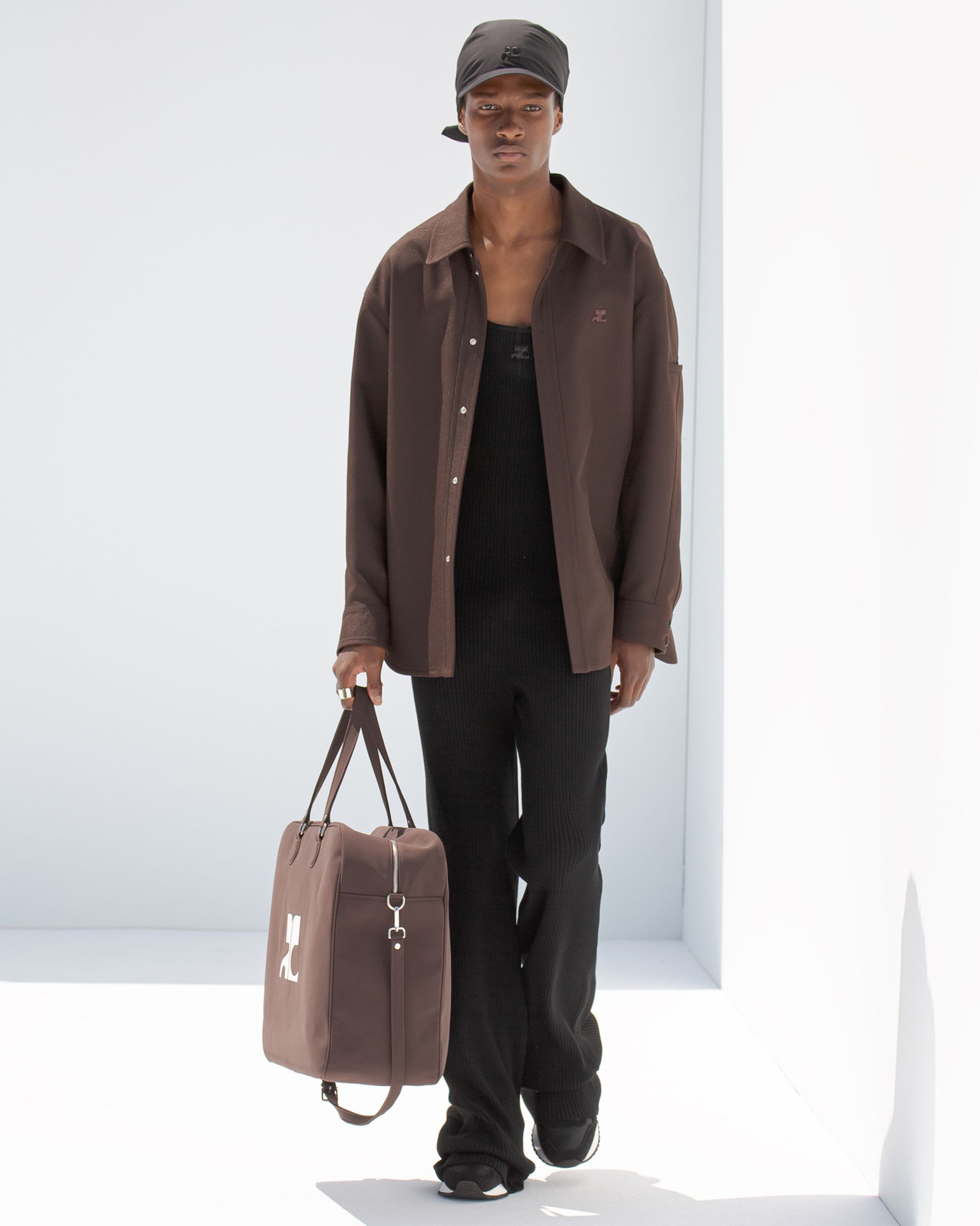 Elegant Courrèges model in black and brown casual streetwear style, carrying a logo-bag.
