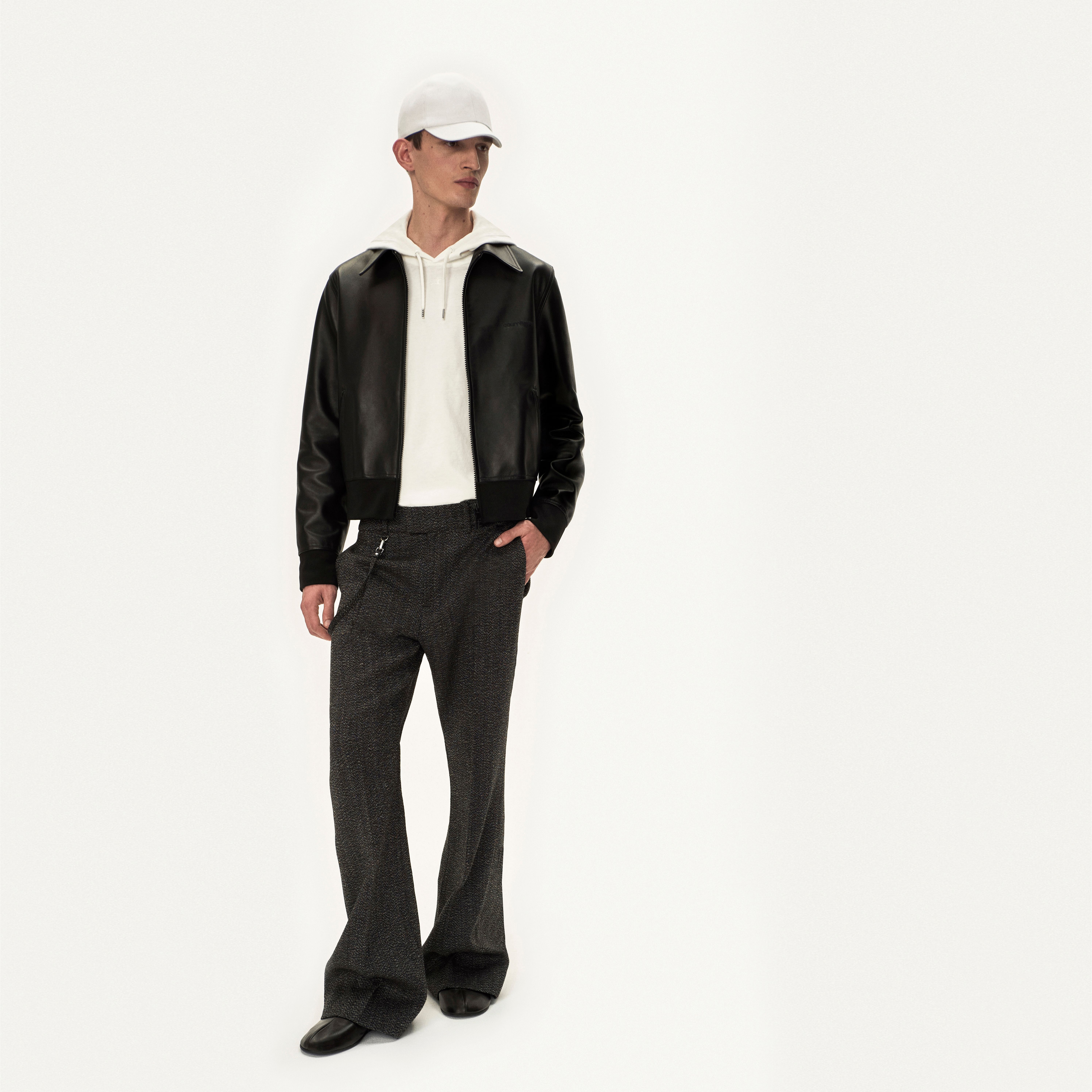 Fashion-forward man in a black leather jacket, white hoodie, and tailored trousers for Courrèges.