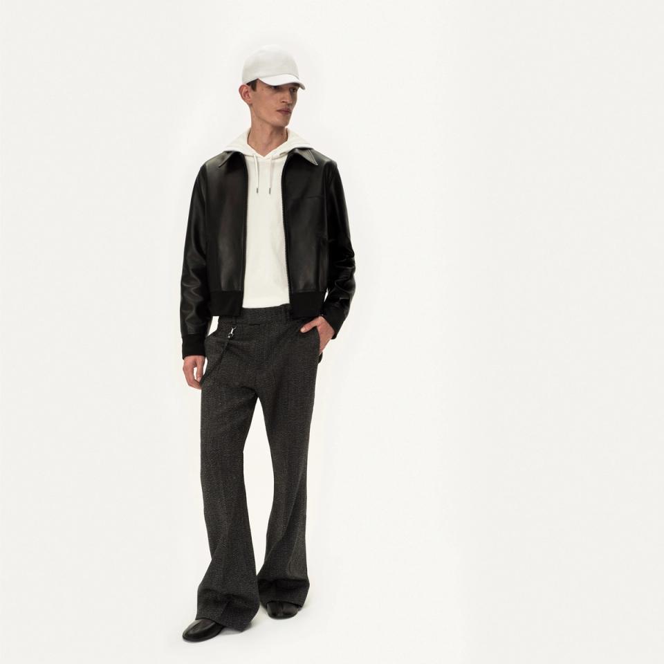 Homme à la mode en blouson en cuir noir, sweat à capuche blanc et pantalons élégants pour Courrèges.