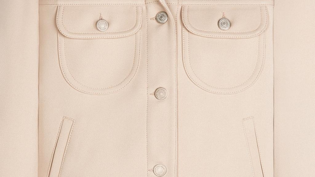 Détail élégant d'une veste beige Courrèges avec couture fine et boutons argentés visible.