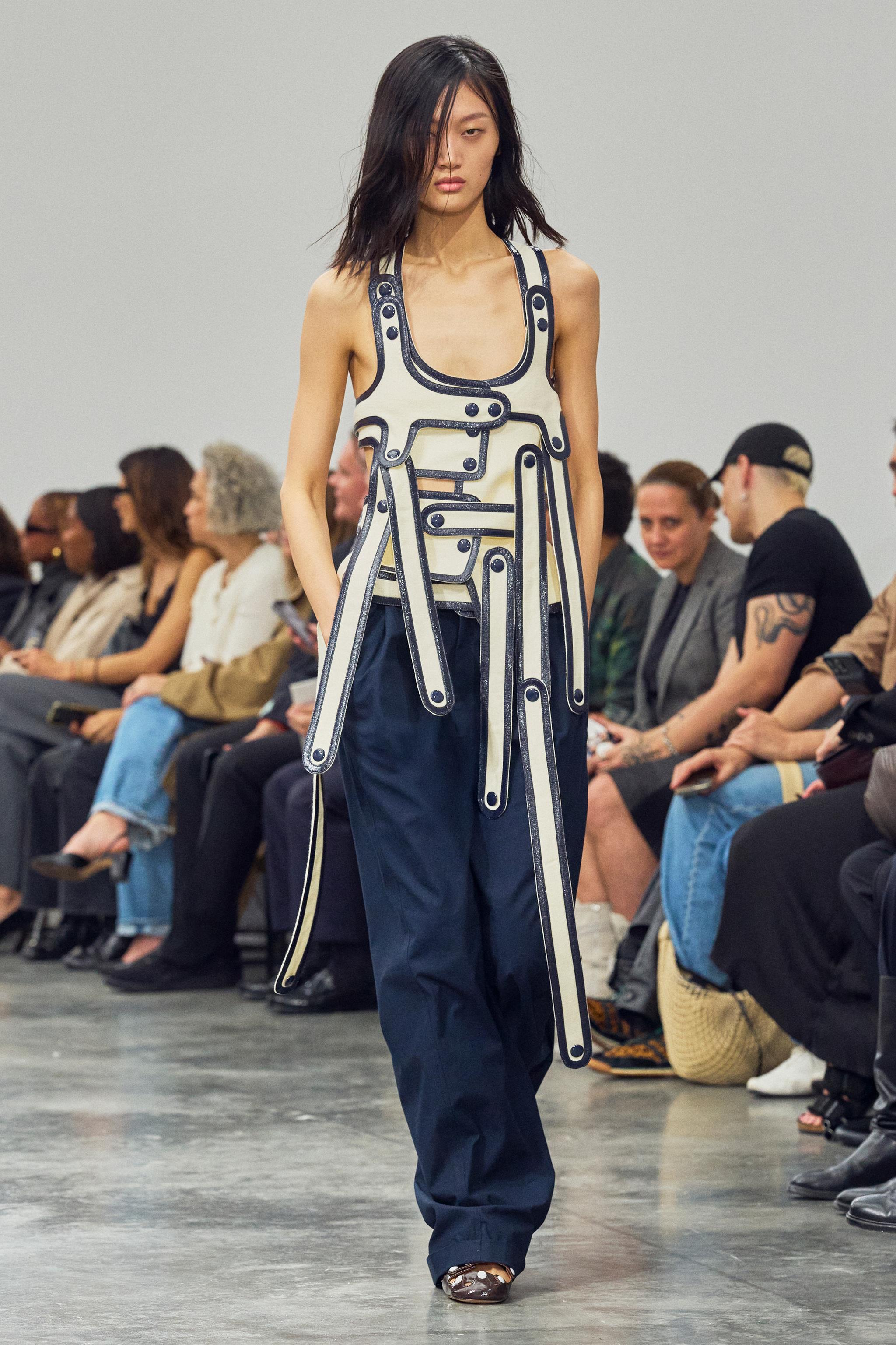 Elegant model wearing Courrèges contemporary fashion on runway, diverse audience in stylish attire.