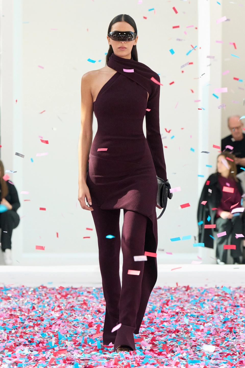 Elegant model in purple Courrèges outfit on runway with colorful confetti, showcasing fashion.