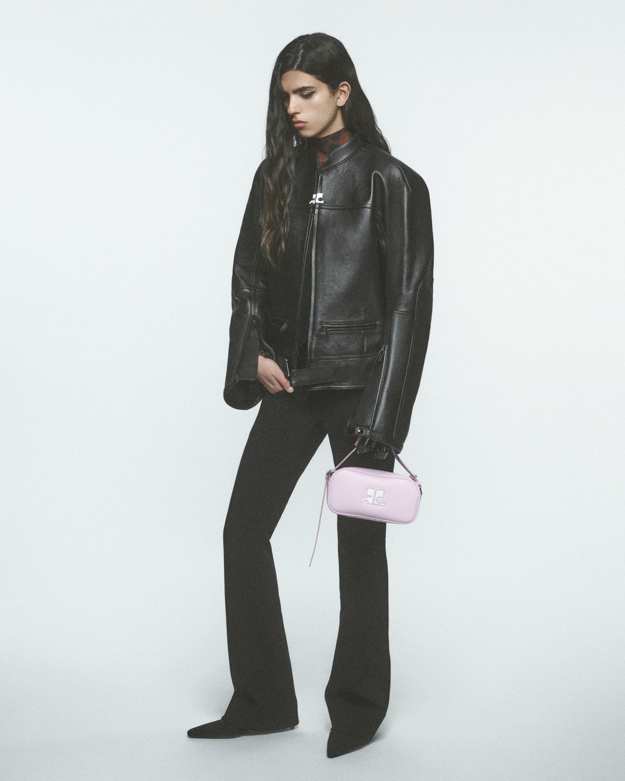 Elegant fashion model in black leather jacket holding a pink Courrèges handbag for ecommerce.