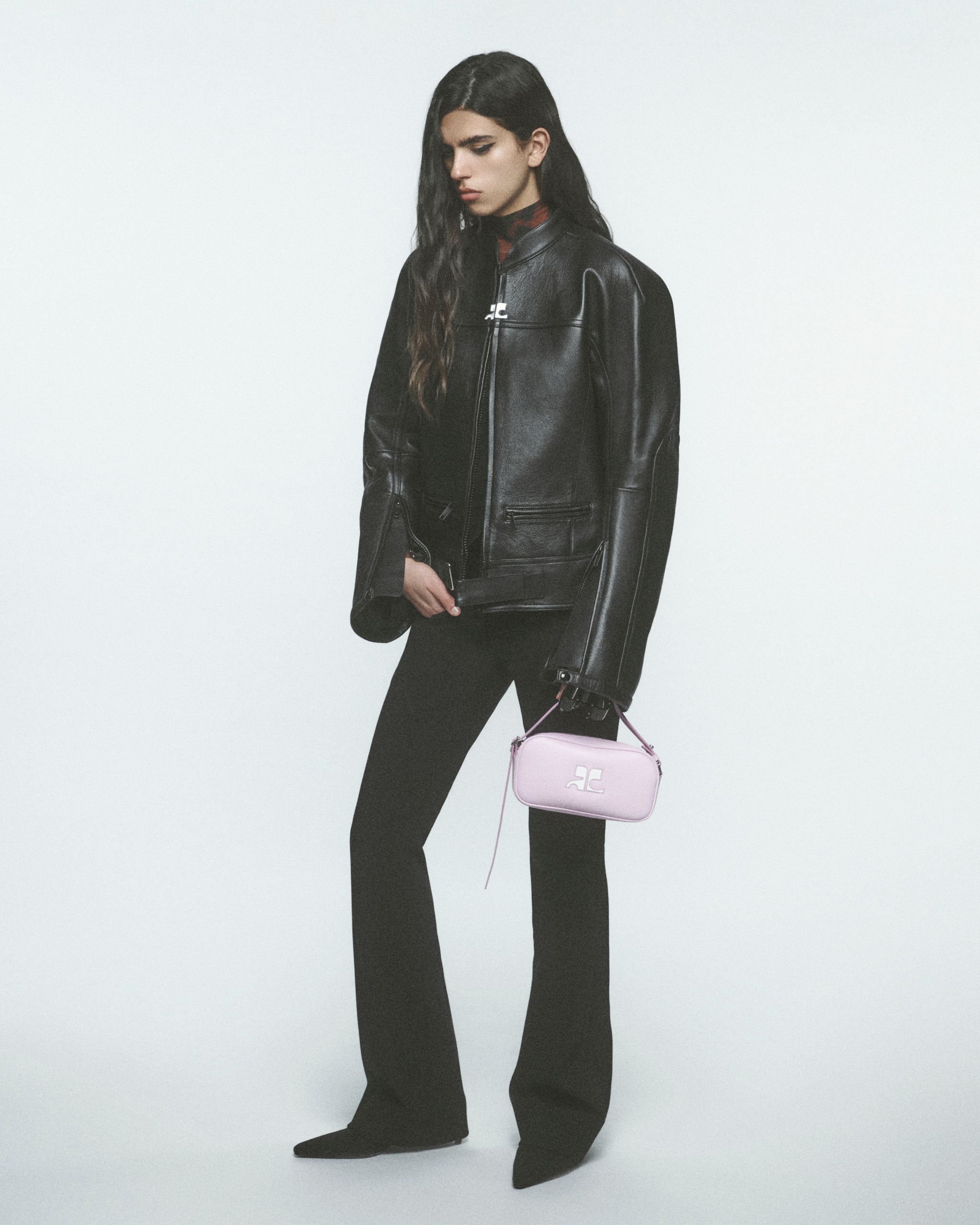 Femme élégante portant une veste en cuir Courrèges noire et un pantalon, avec un sac pastel rose.