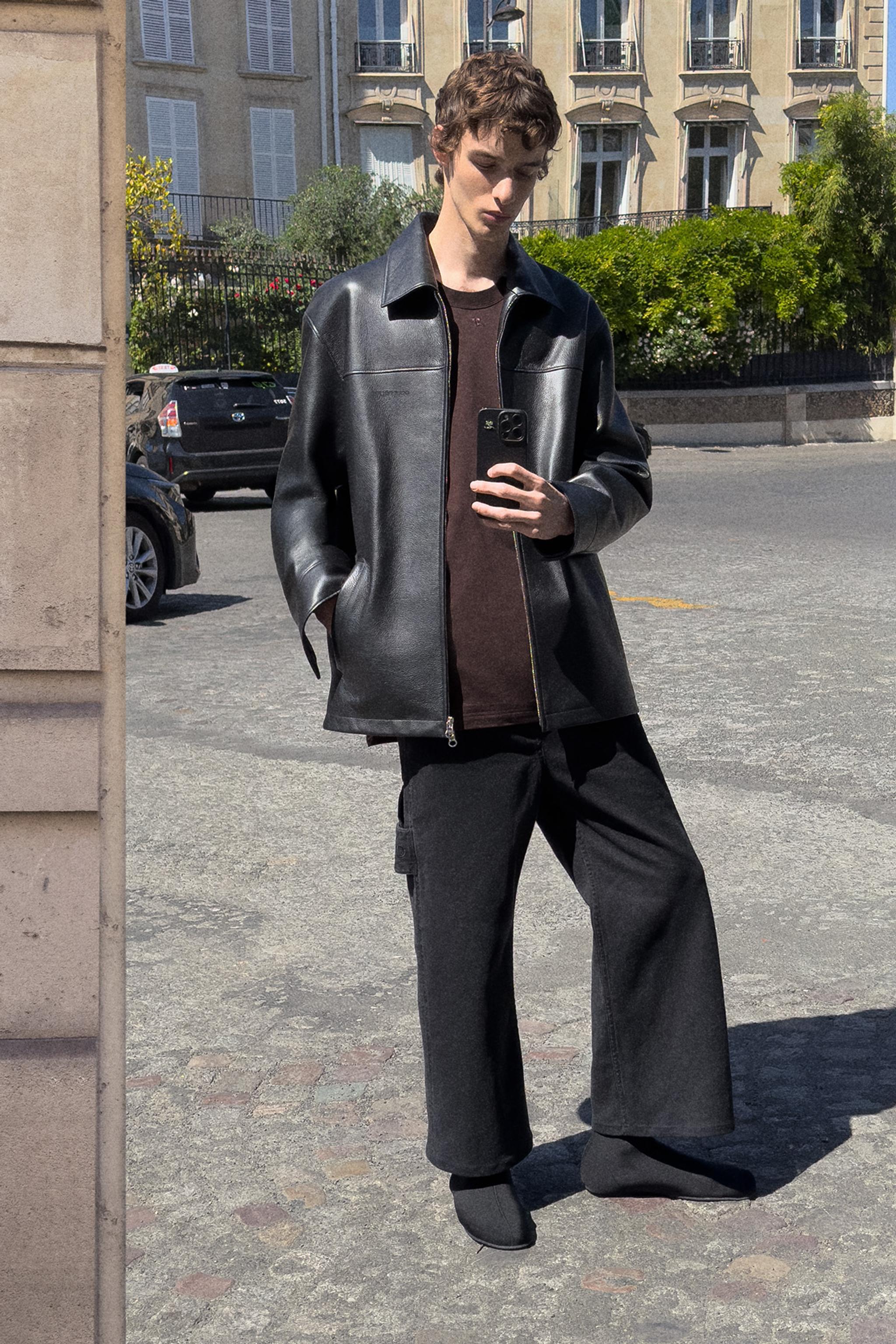 Elegant black leather jacket and wide-leg pants modelled on a city street for Courrèges.