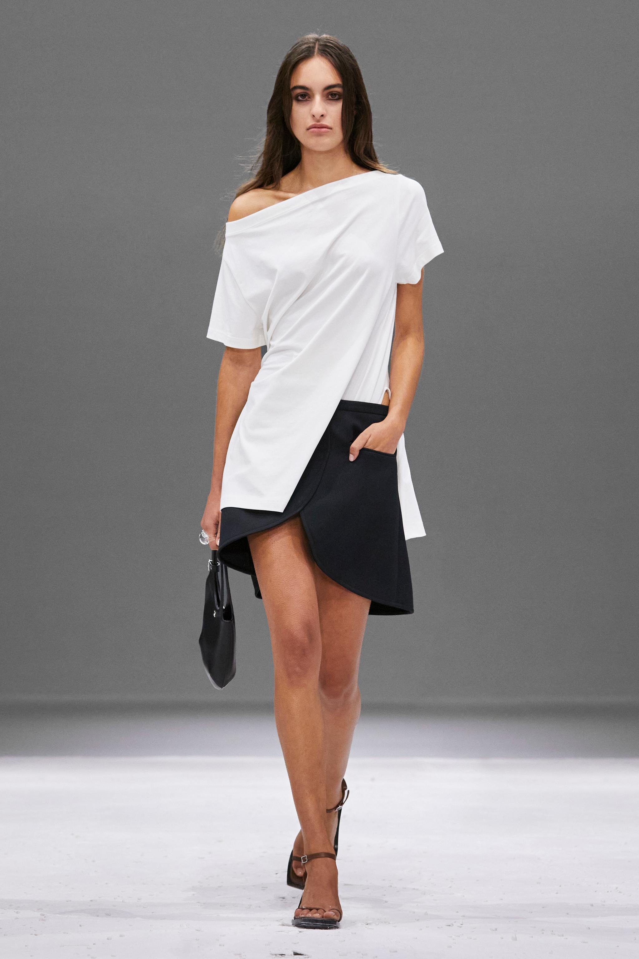 Elegant model wearing white top and black skirt by Courrèges on a runway for an ecommerce site.