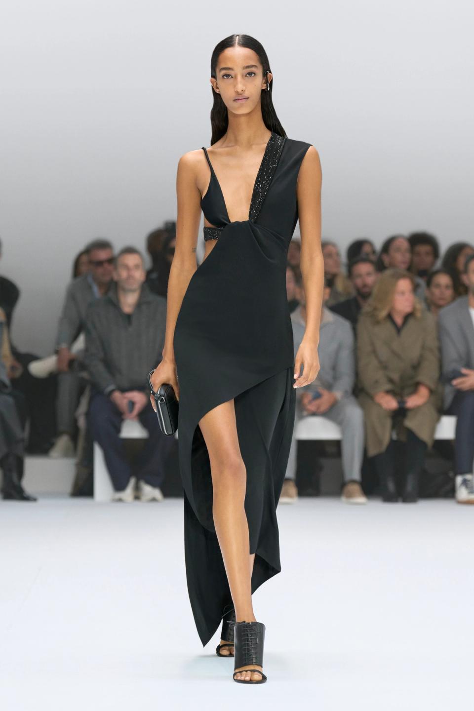 Elegant black dress showcased on a runway for Courrèges, featuring asymmetrical design and high slit.