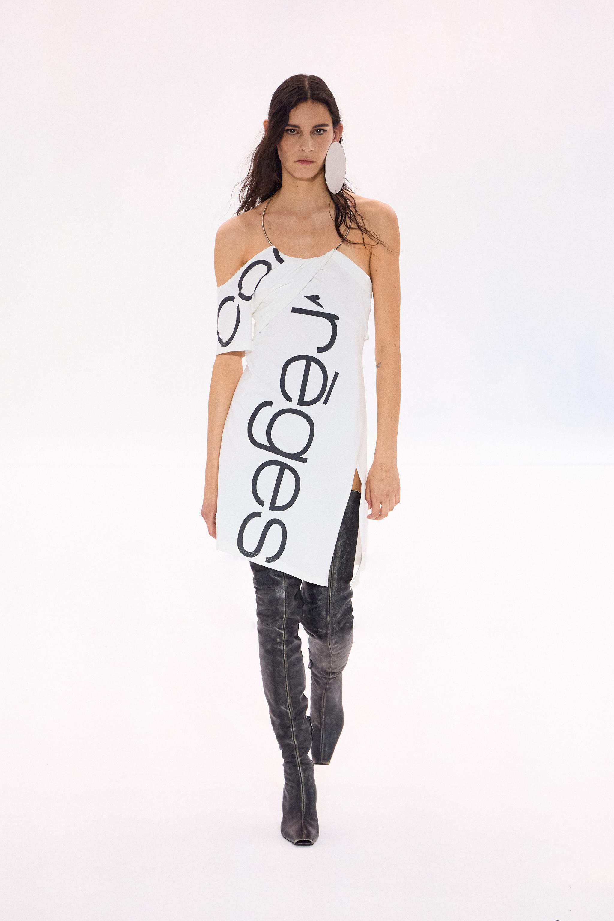 Elegant fashion model in a white Courrèges dress with black text, showcasing modern style.