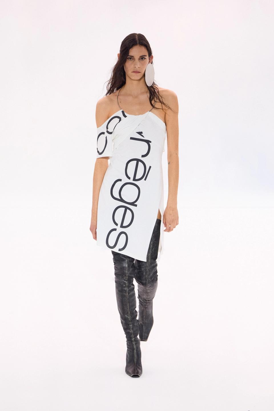 Elegant fashion model wearing a Courrèges white dress with bold black logo, modern style.