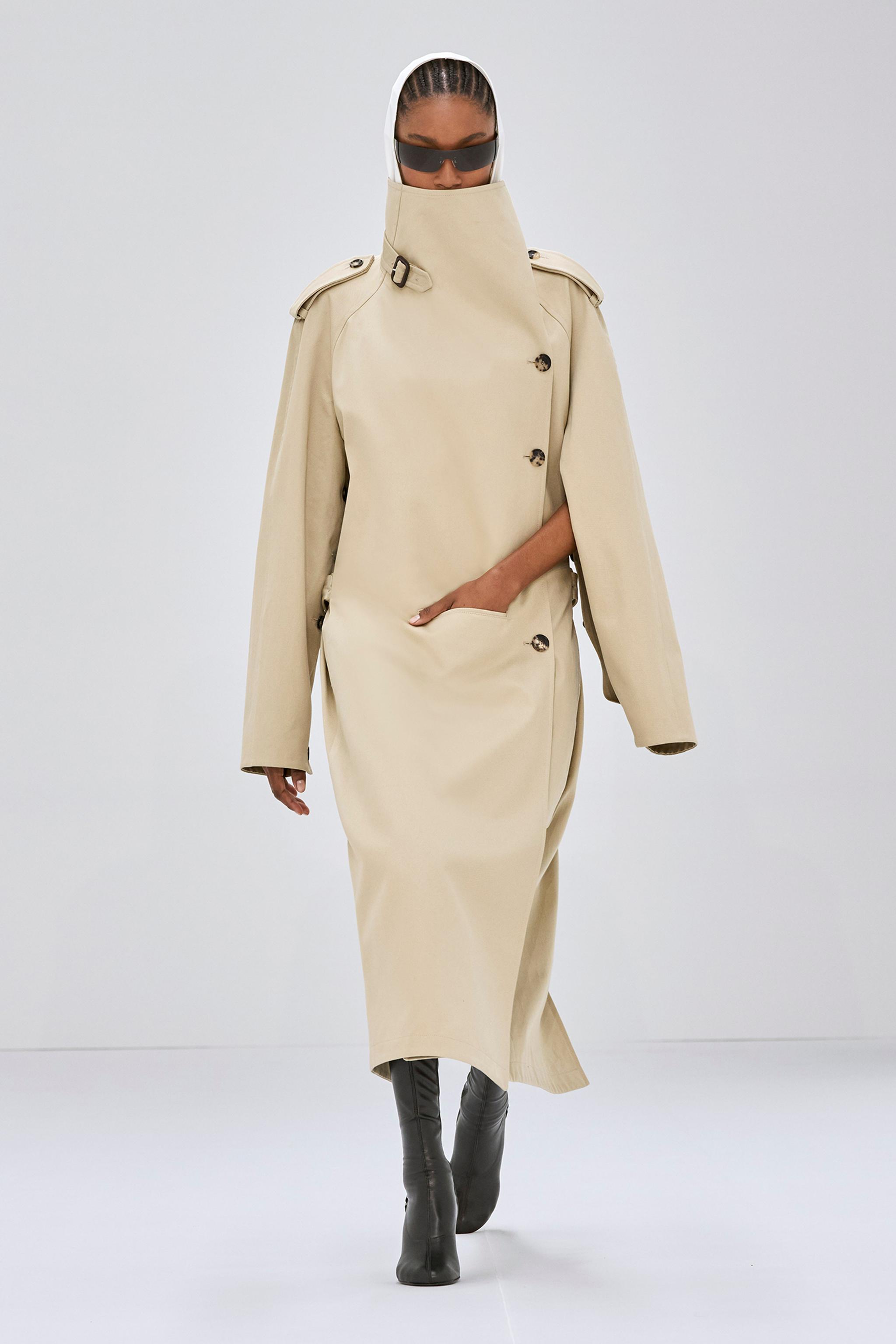 Manteau trench beige élégant avec col haut, détails modernes et coupe sophistiquée de Courrèges.