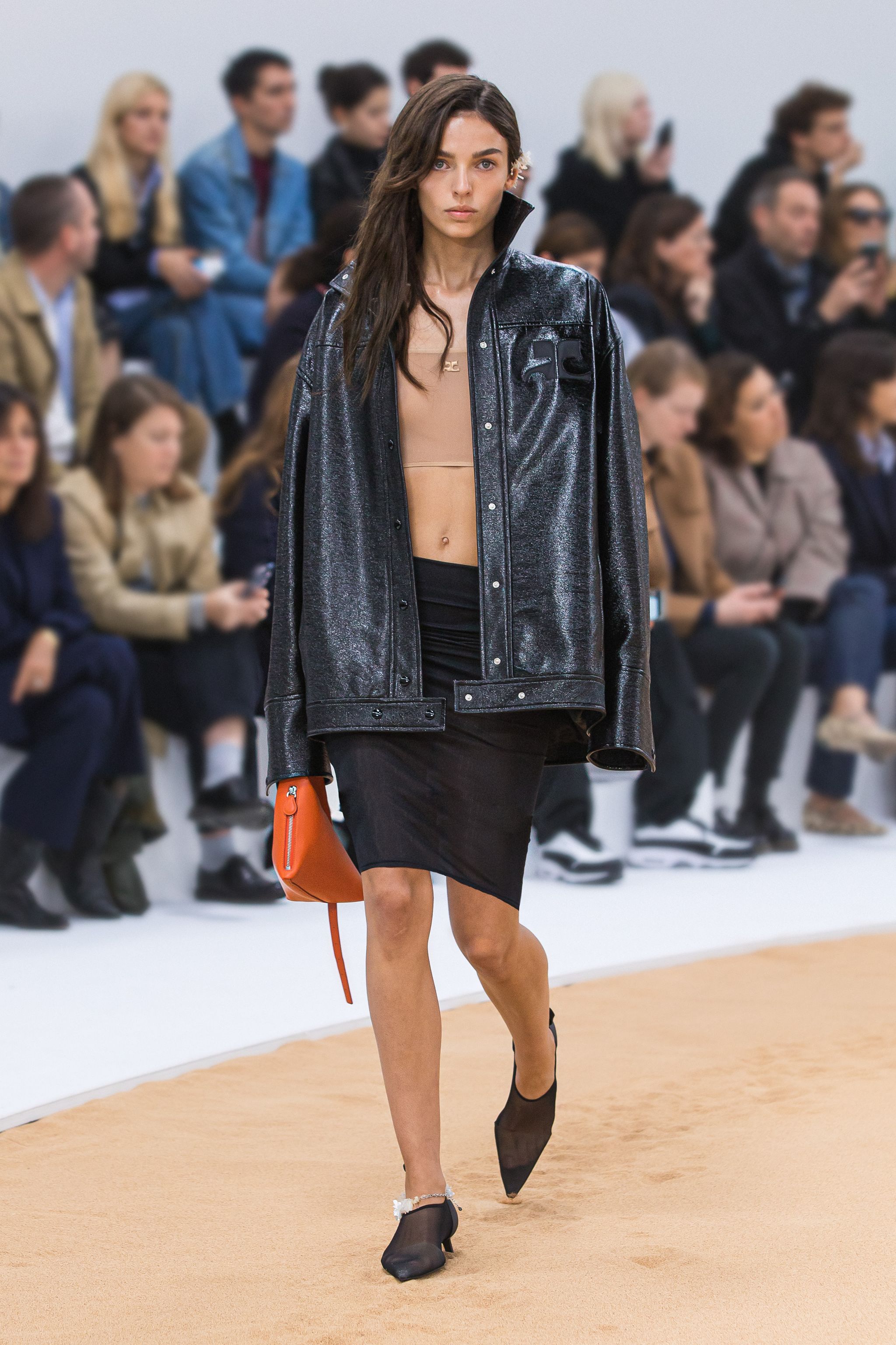 Elegant fashion runway model wearing Courrèges black shiny jacket and stylish accessories.