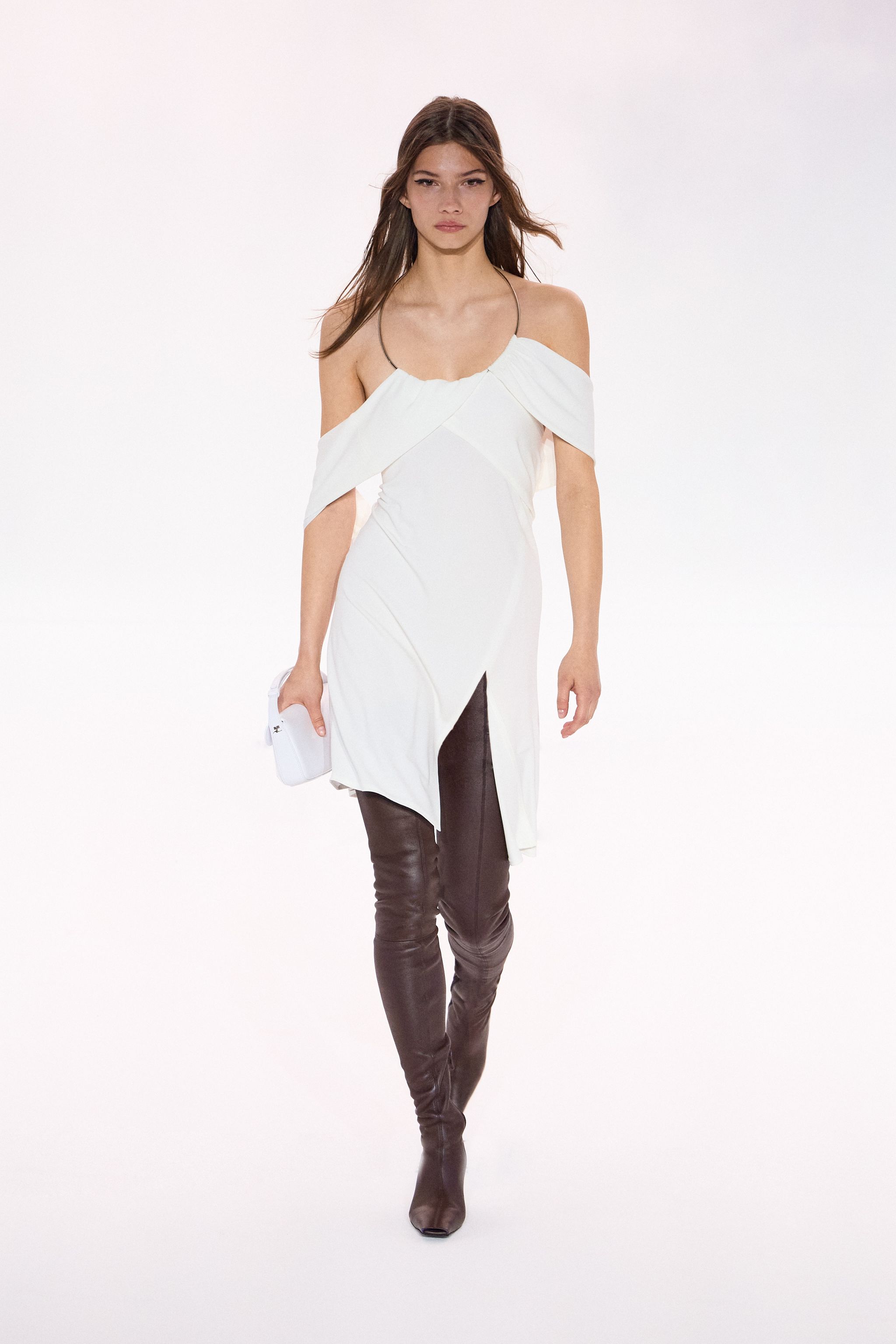Elegant white Courrèges dress with off-shoulder design, paired with black leather thigh-high boots.