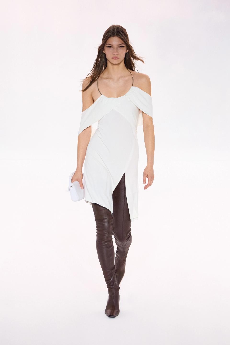 Elegant white Courrèges dress with off-shoulder design, paired with black leather thigh-high boots.