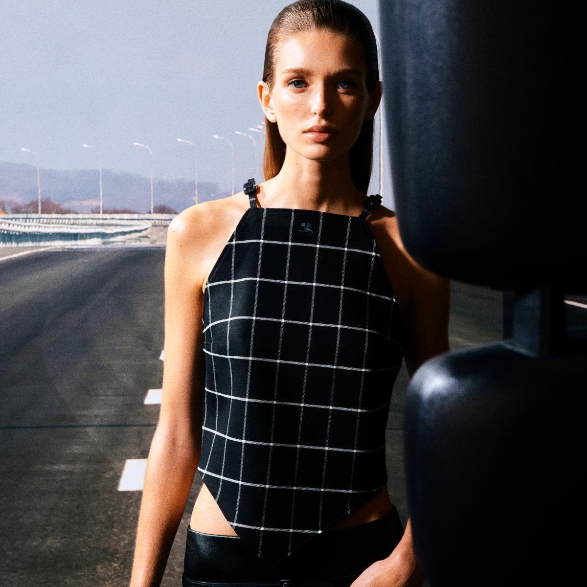 Elegant Courrèges fashion model in black checkered top on a modern road backdrop.