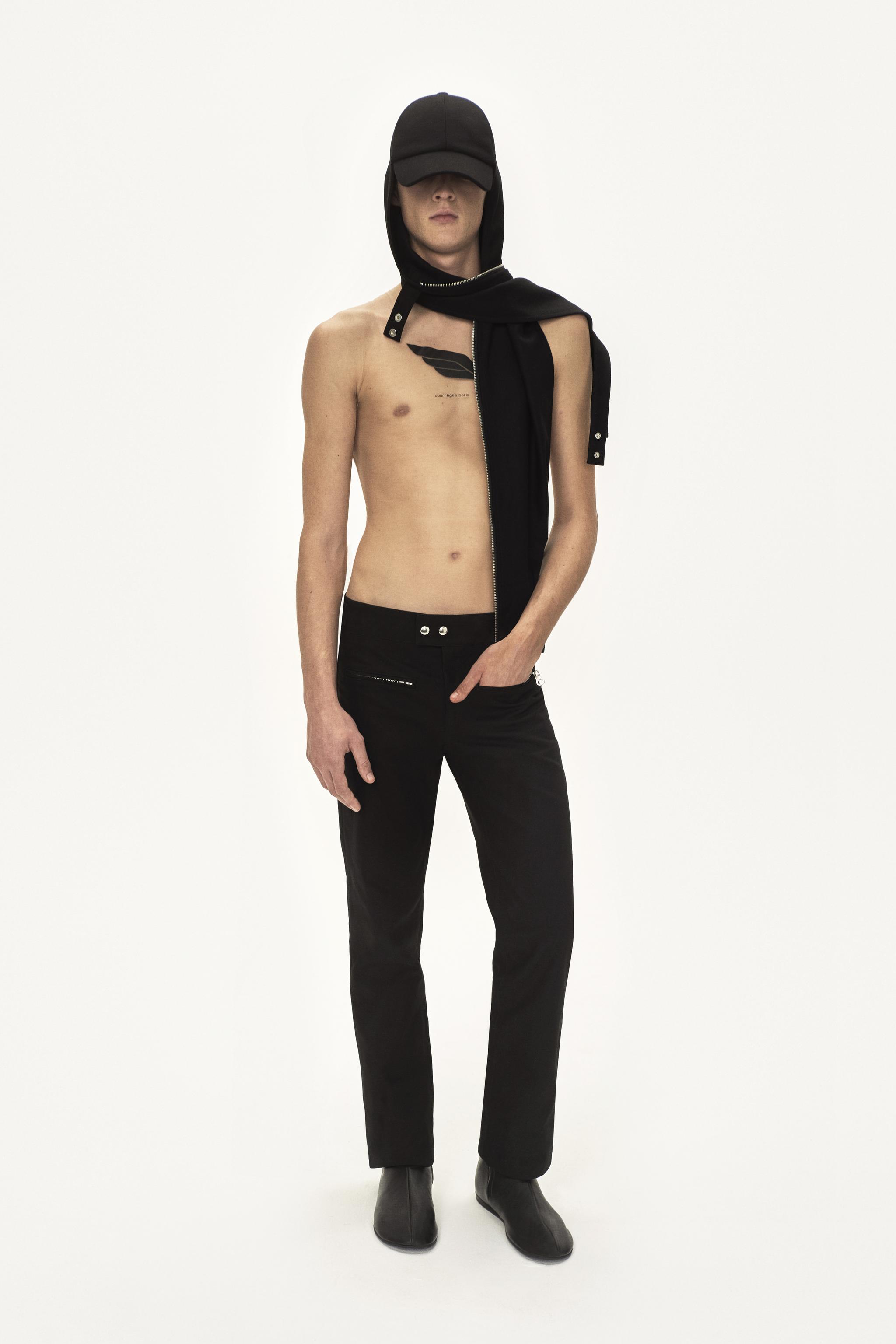Modèle masculin élégant portant un pantalon noir Courrèges, veste à capuche et casquette pour un look tendance.