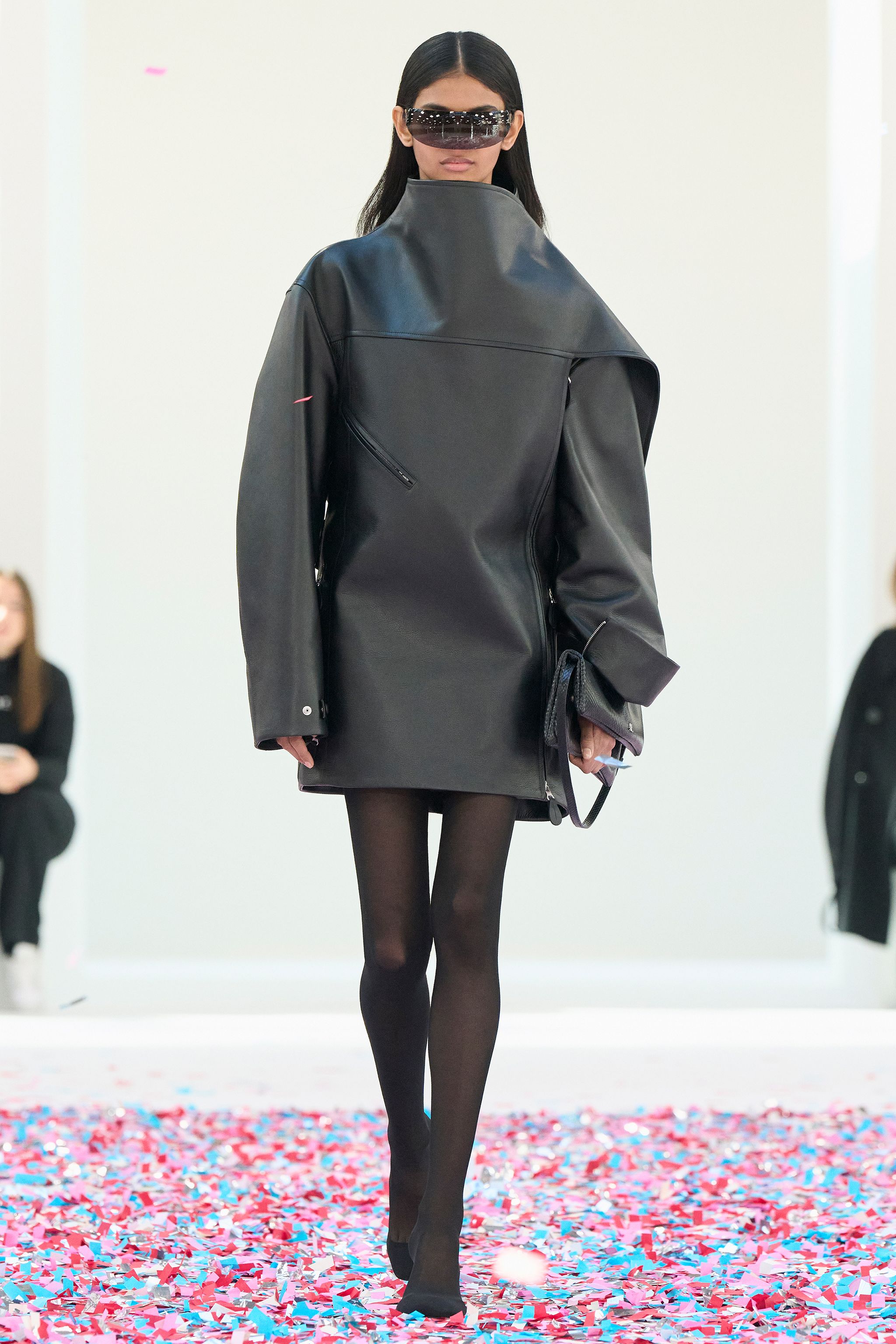 Elegant black leather oversized coat with high collar and stylish detailing, on a runway.