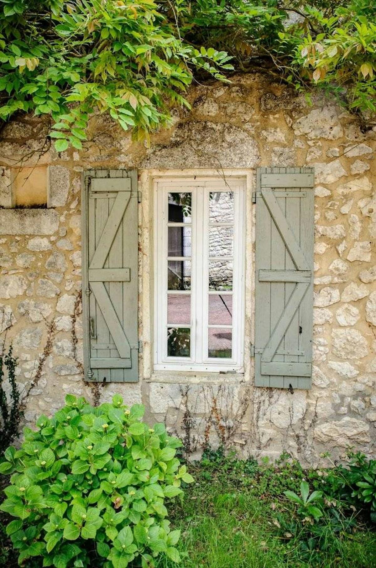 Une fenêtre aux volets vert-de-gris dans la façade de calcaire