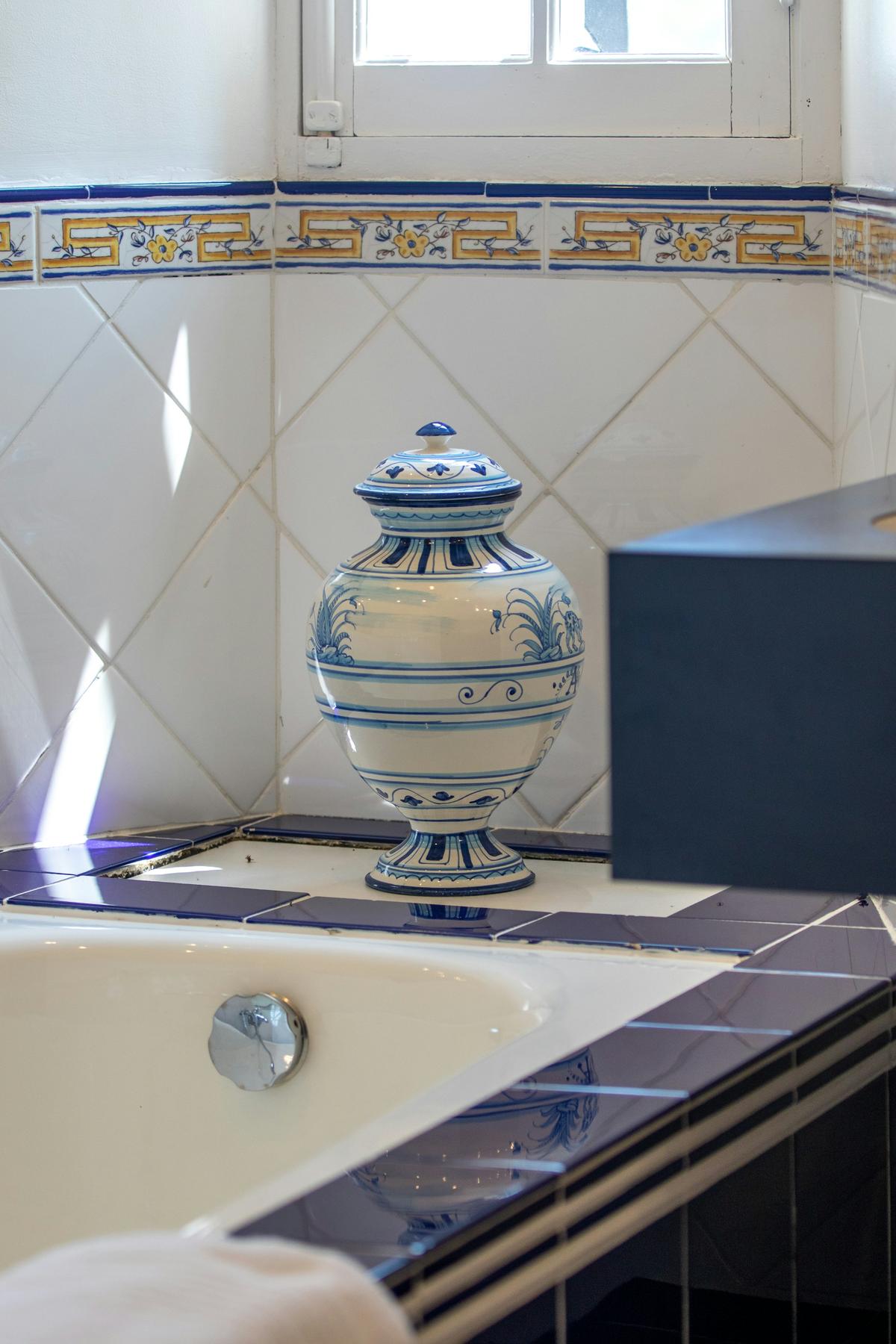 Une urne en céramique bleue et blanche sur le rebord carrelé d’une salle de bain