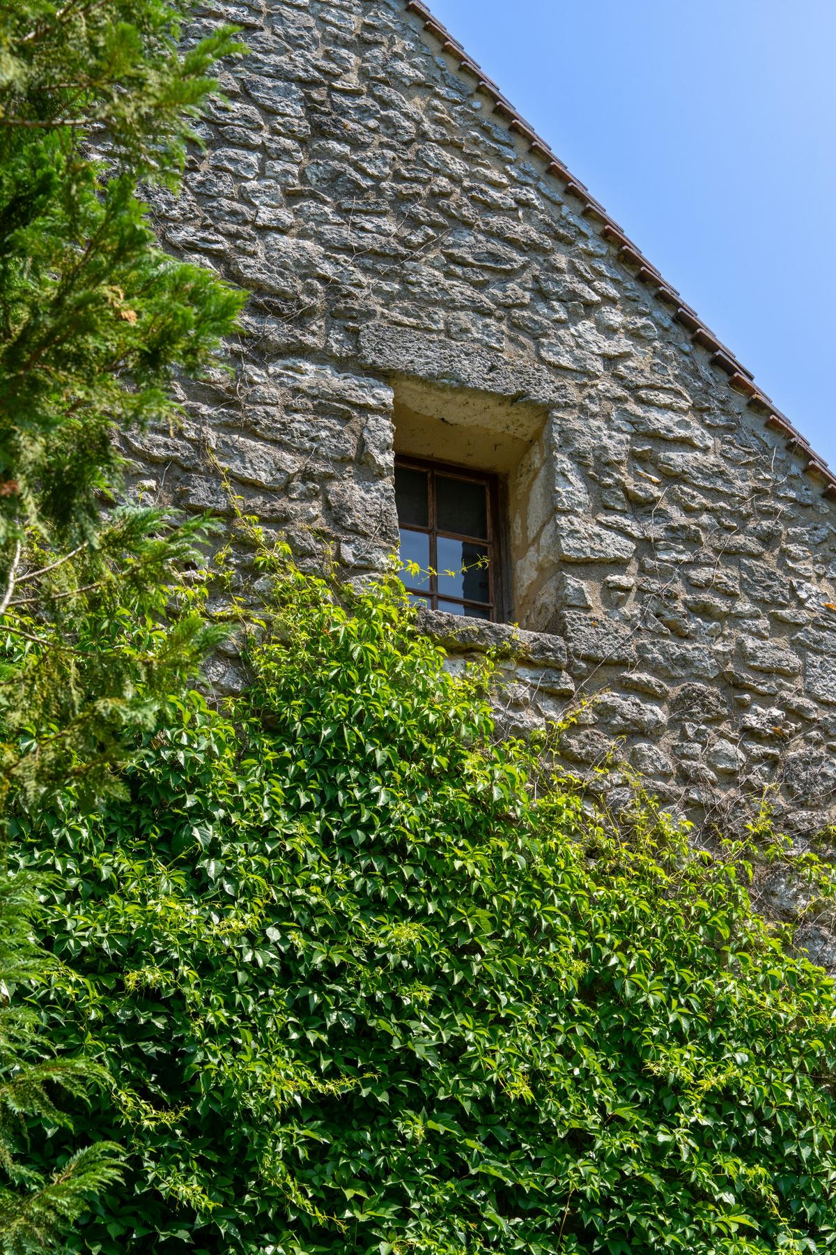 Un mur de pierre et une petite fenêtre sous la verdure