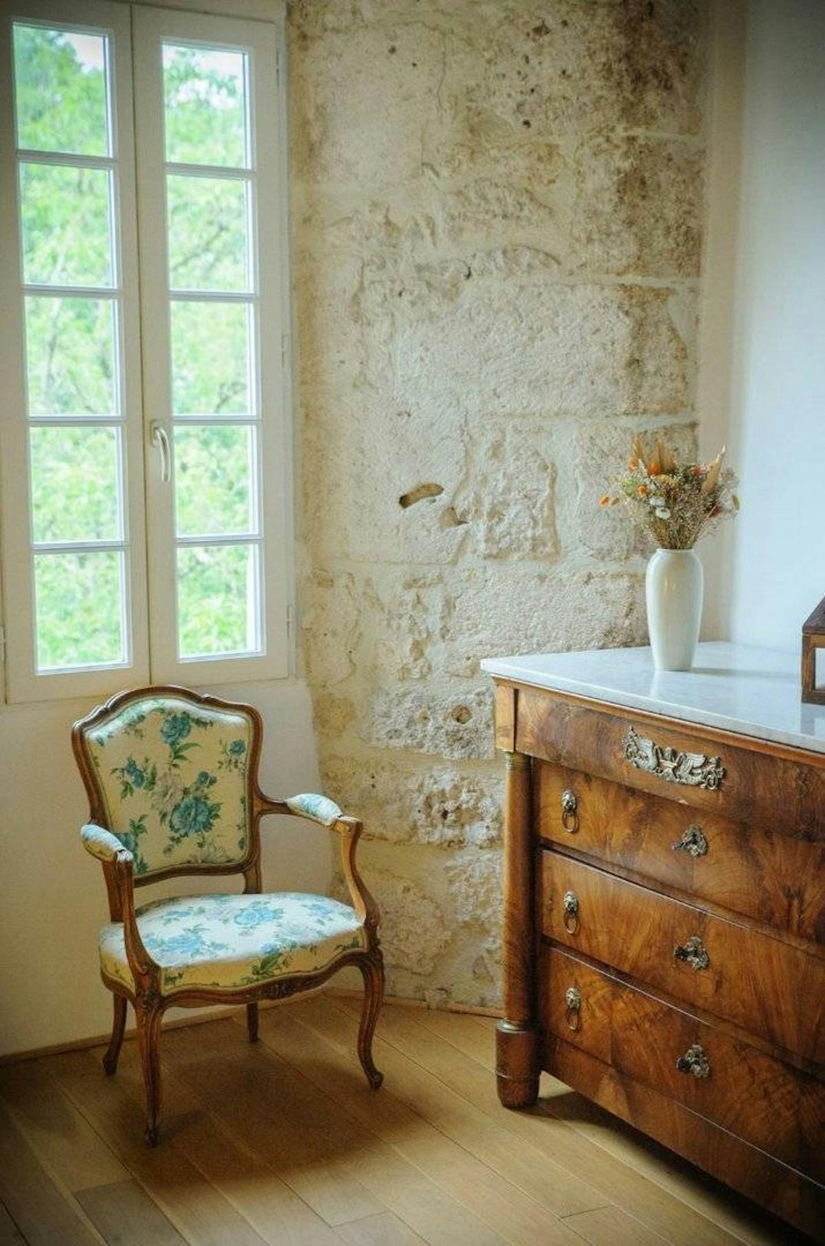Un coin de chambre avec une chaise d’époque, une commode et des fleurs séchées