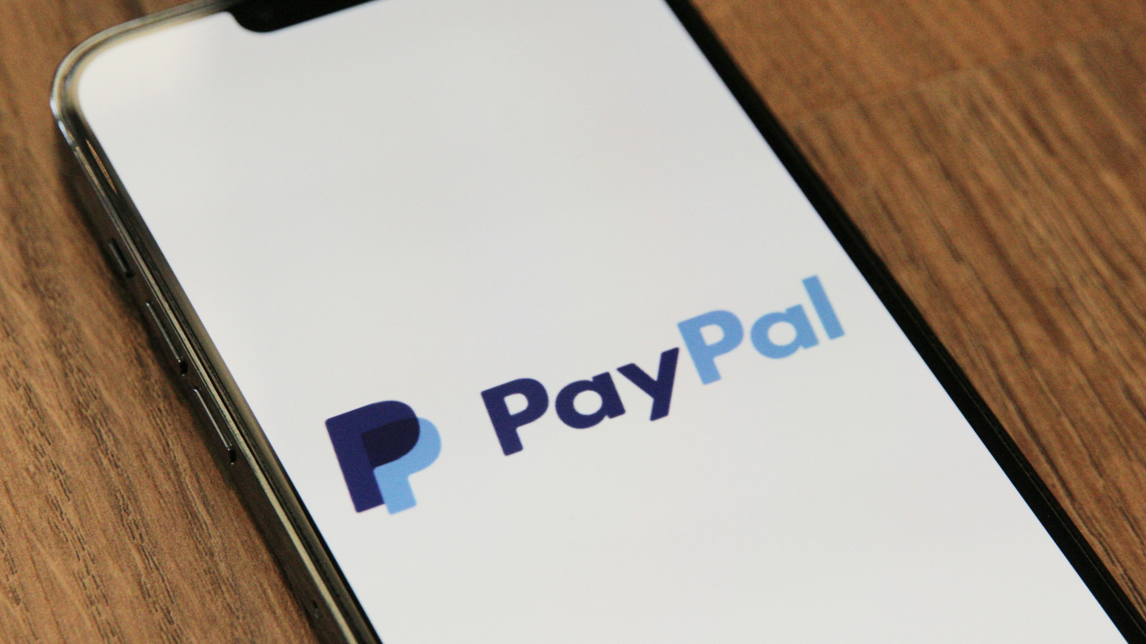 a cell phone with the paypal logo on the screen is sitting on a wooden table .