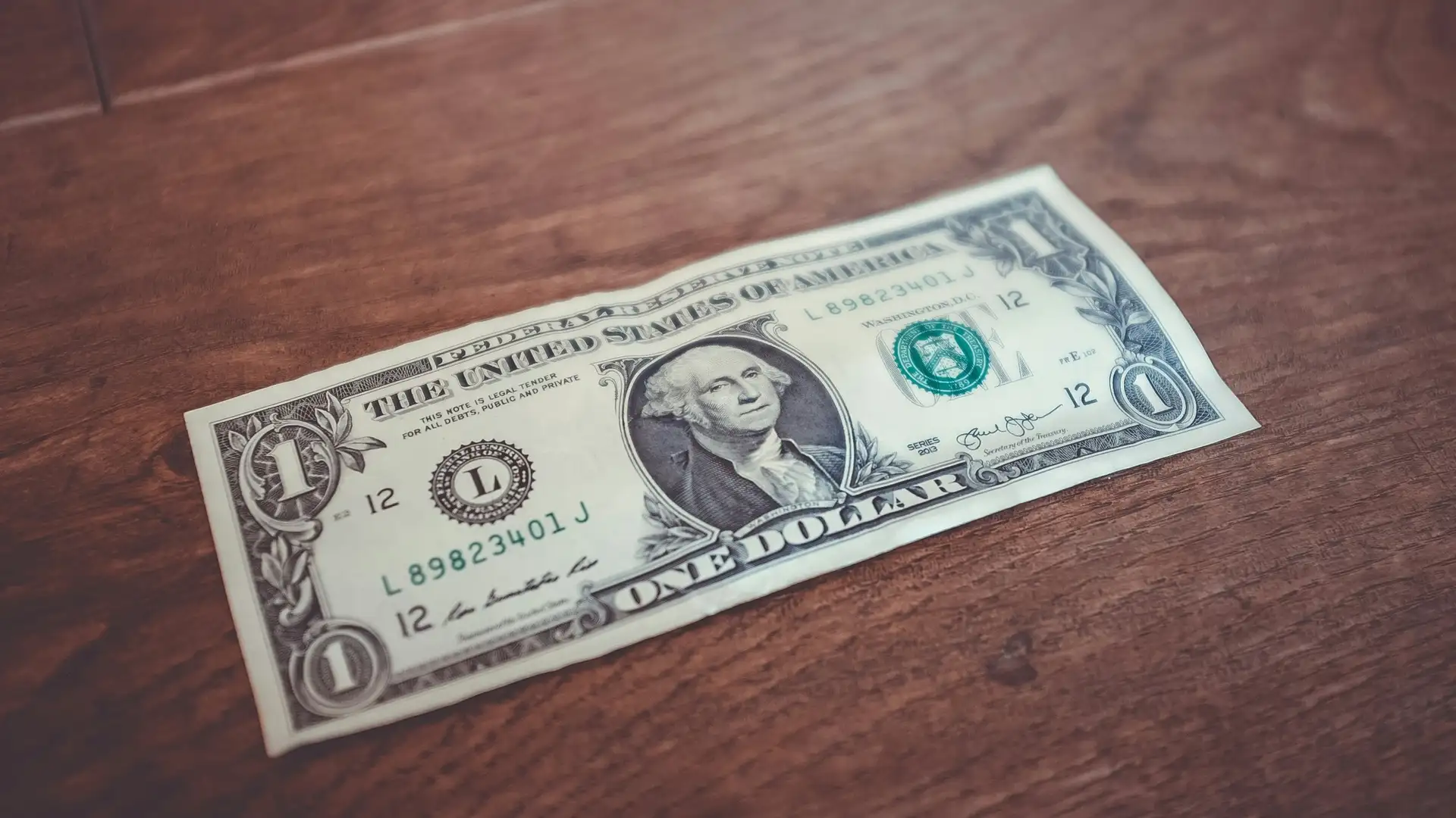 A one dollar bill is laying on a wooden table.