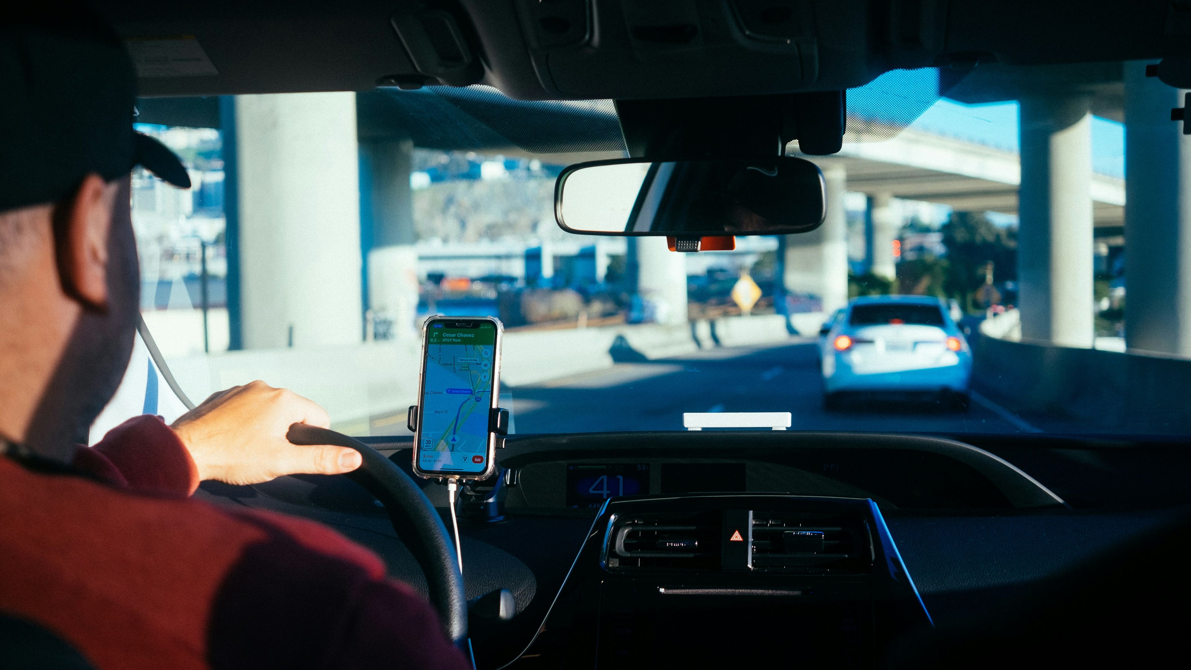 a man is driving a car on a highway while using a cell phone .