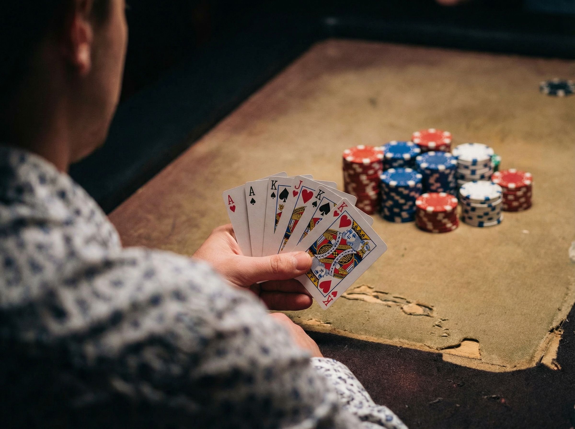 A person showing their cards while playing poker, with gambling chips are in the background.