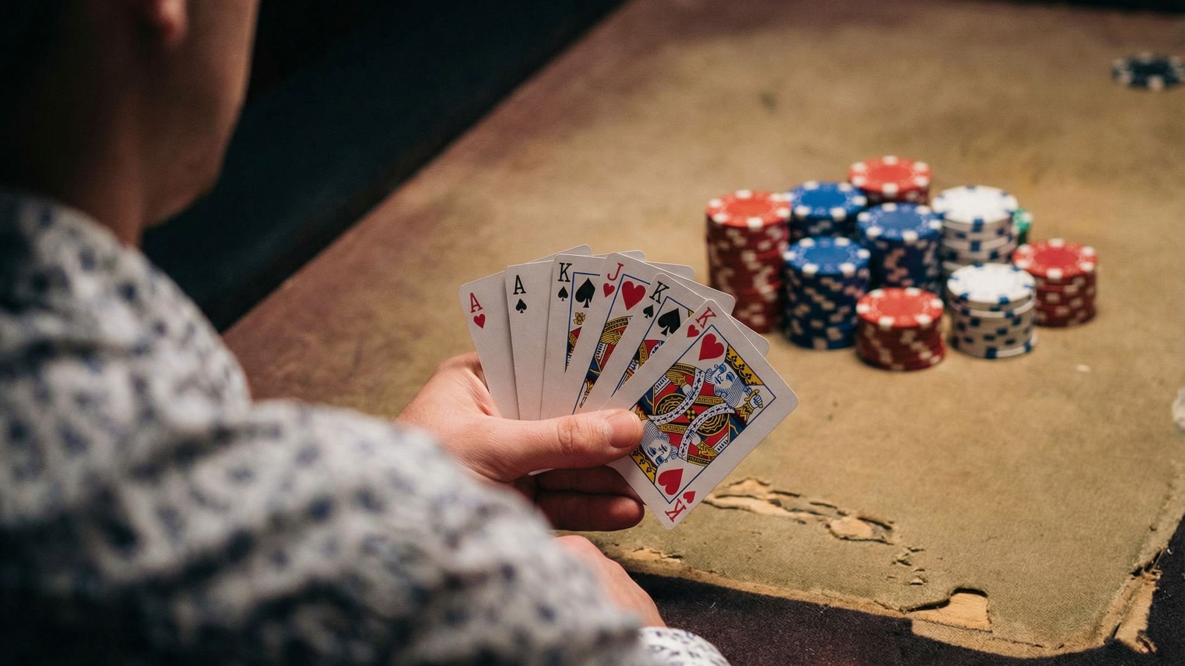 A person showing their cards while playing poker, with gambling chips are in the background.