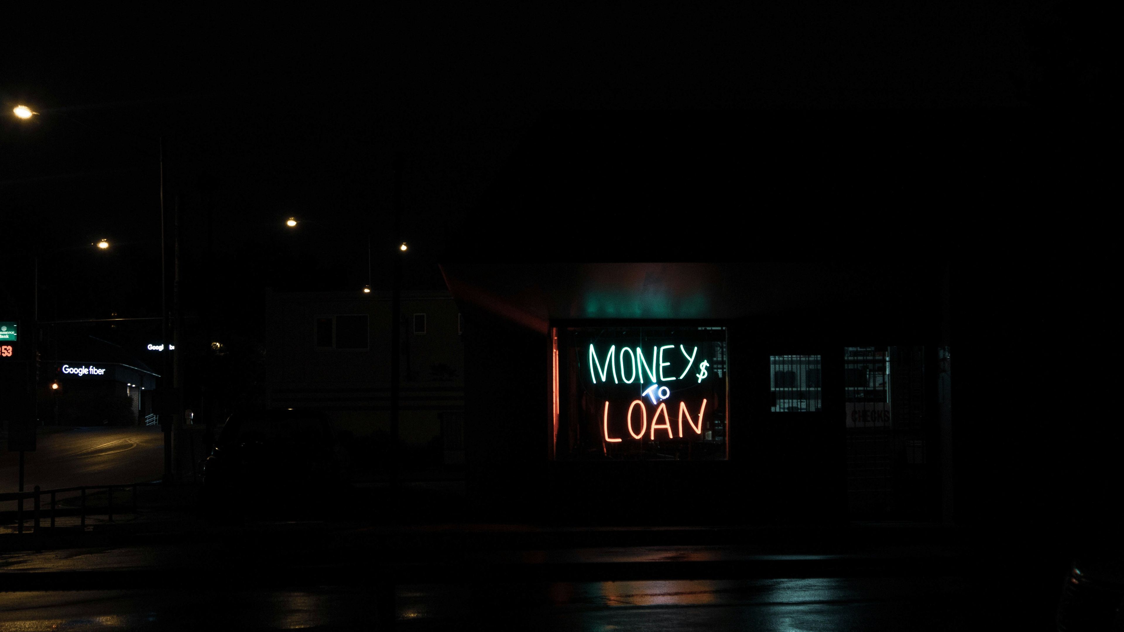 a neon sign for a money and loan store is lit up at night .