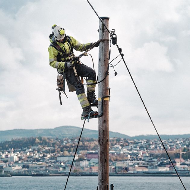Montør i toppen av en strømstolpe med Trondheim i bakgrunnen