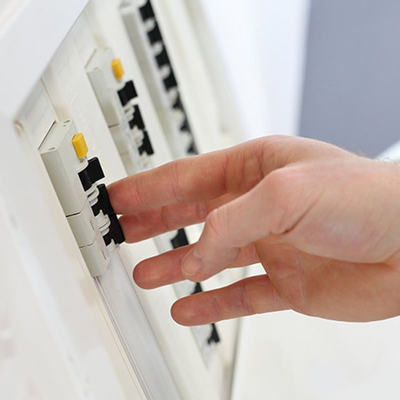 Nærbilde av et sikringsskap. En hånd holder fingrene på to av automatsikringene.