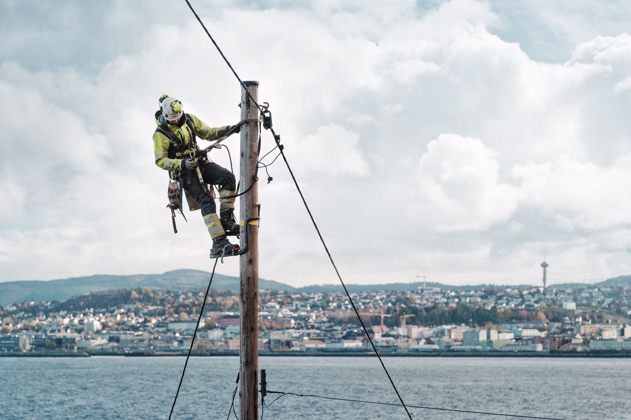Montør som klatrer i en strømstolpe med Trondheim i bakgrunnen