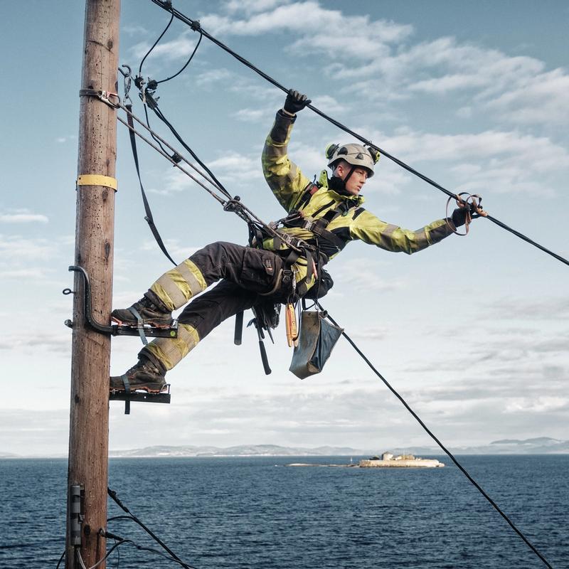 Montør som klatrer i en strømstolpe med fin utsikt i bakgrunnen
