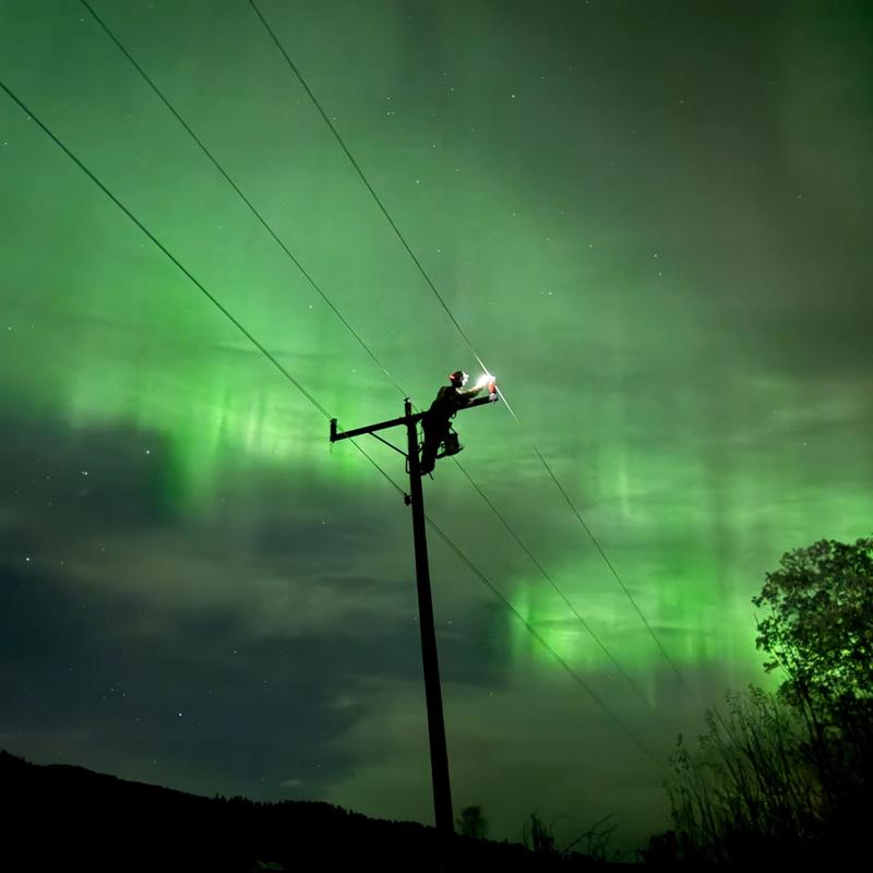 Montør ute på natten i vakkert nordlys for å fikse feil i strømnettet