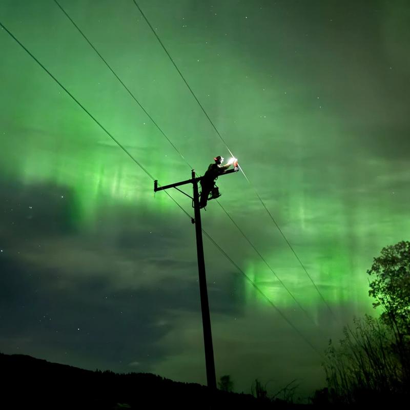 Montør ute på natten i vakkert nordlys for å fikse feil i strømnettet