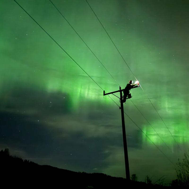Montør ute på natten i vakkert nordlys for å fikse feil i strømnettet