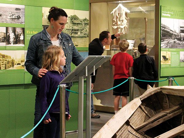 A mother and young child explore a maritime exhibit featuring a historic wooden boat at the Coos History Museum in Coos Bay, Oregon.