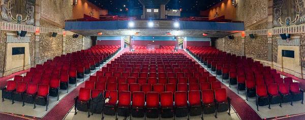The grand auditorium of the Egyptian Theater in Coos Bay, viewed from the stage, with rows of red velvet seats, Egyptian-themed wall murals, and a mezzanine level above.