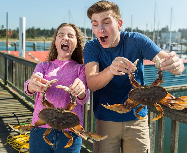Two teenagers laughing and holding Dungeness crabs on a dock at Charleston Marina.