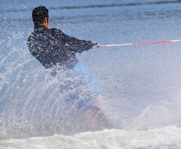 Man in a wetsuit gripping a tow rope while water skiing through heavy spray.