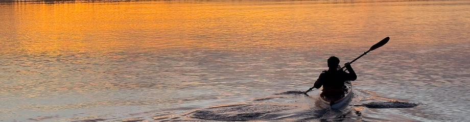 Silhouette of a kayaker paddling across calm water at sunset on Sunset Bay.