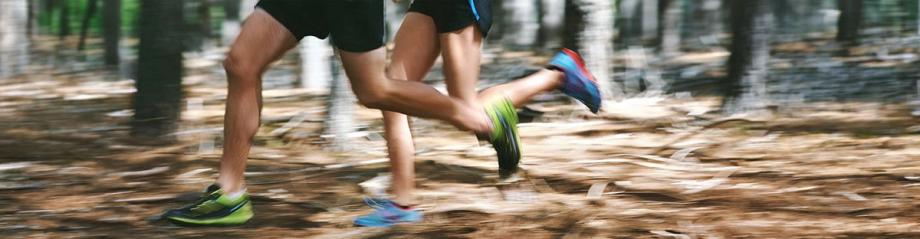 Close-up of two runners' legs mid-stride on a wooded trail during the Sunset Trail Run.